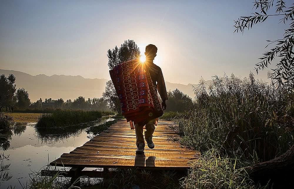 A rug vendor sets out at sunrise in the interiors of Dal Lake in search of customers.