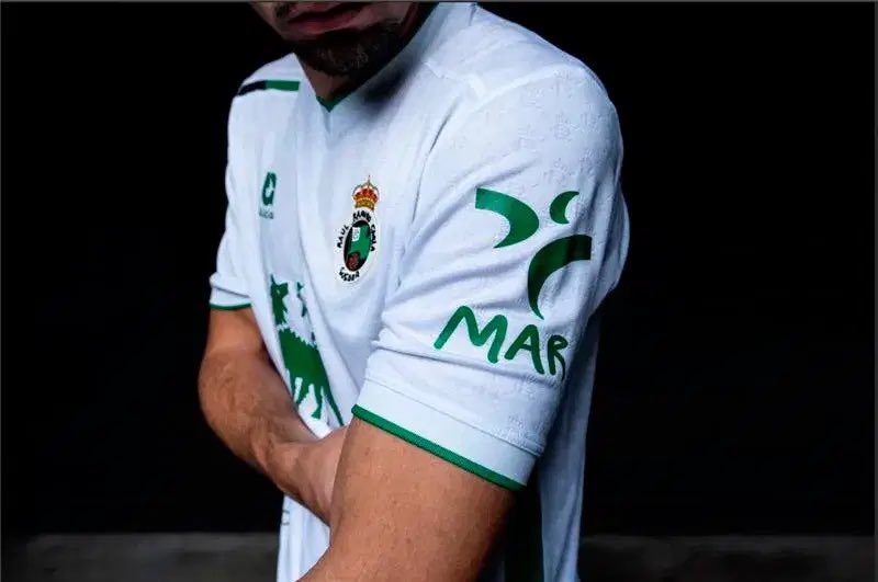 Hay campañas que te hacen mirar dos veces una camiseta.
El Racing de Santander salió al campo y… algo faltaba.
Los logos de sus patrocinadores habían desaparecido.