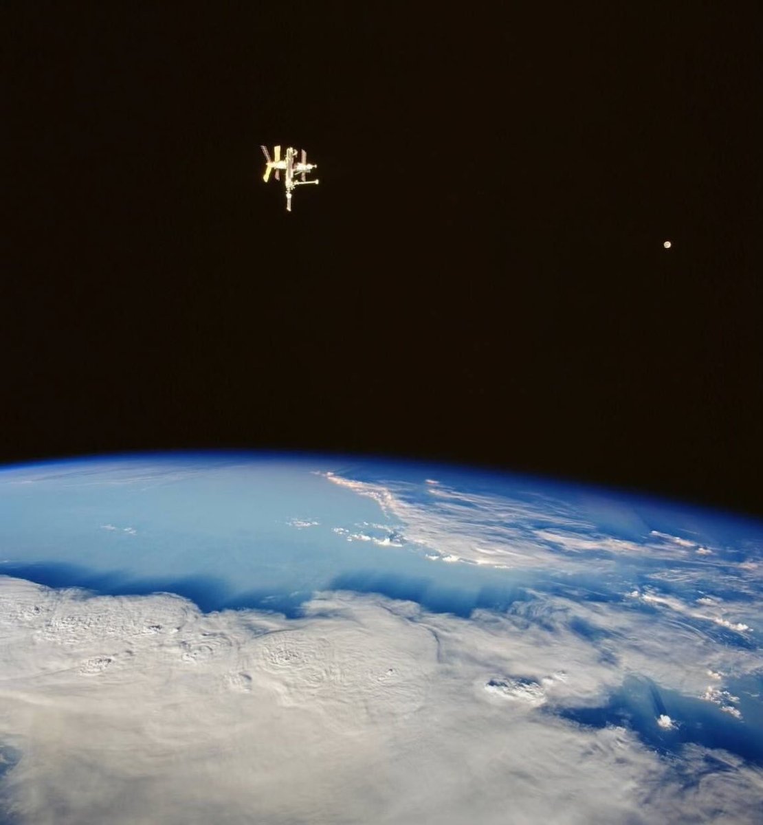 This is a beautiful and historically significant photograph!
It shows the Russian space station Mir silhouetted against the Earth’s limb, with the Moon visible in the background, taken from Space Shuttle Discovery during the STS-91 mission in June 1998.
Key details:
•The bright