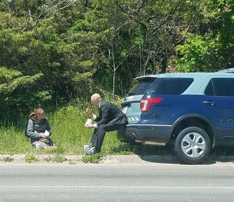 HumanityChad's tweet photo. Sometimes we need an old story to restore our faith in humanity.

"Mother of four Lynn Murphy was panhandling in Massachusetts, asking for money from drivers, when a state police officer pulled up to her. Initially, he just drove past her. But he came back with food for her that he had picked up at a nearby restaurant. The woman thought he was stopping to give her a ticket for panhandling, but he gave her the food instead. However, he didn’t just leave it with her. He asked her to come around to the back end of his cruiser and he sat on the bumper and ate with Lynn, having something of a picnic.

That police officer was Luke Bonin and a passerby took a photo of the two eating together and posted it to Facebook. It has been shared more than 100,000 times.

Says Lynn: “I thought he was just going to hand me the meal but when he said: “Come around the back, it’s such a beautiful day, we’ll have a picnic,’ I thought that was… it touched my heart.”

The state police department also posted the photo on their website, and explained it with this: “He very reluctantly told us how he ended up sitting on his cruiser’s bumper that day sharing lunch with a stranger. Trooper Bonin had just left court when he drove by the woman, who appeared down on her luck. She was holding a sign and asking for help from anyone who would pay attention.

Trooper Bonin continued to drive on – directly to a local establishment, where he ordered two meals. He returned to the woman, pulled up, and exited his cruiser. Thinking he was there to remove her from the side of the road, she immediately stated to him that she would leave, that she knew she shouldn’t be there with her sign. But Trooper Bonin told her, “I’m not here to kick you out.” He then extended the two meals and told her to pick one.

They then sat, shared a meal, and a conversation.

Yes, Trooper Bonin, we know you do not want or expect publicity. We know you didn’t want to be noticed, but you were, and the job is proud of you. We commend you for your selfless act, and for “doing the right thing” for someone less fortunate than most people.

We have extraordinary troopers on the Massachusetts State Police who conduct themselves honorably, and perform selfless acts, every day. Most times, it goes unnoticed. But not this day.”

Photo courtesy: Massachusetts State Police