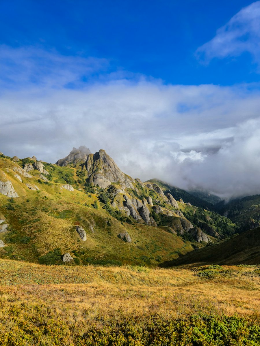 Worldpick13's tweet image. Rolling hills and rocky peaks under a cloudy blue sky