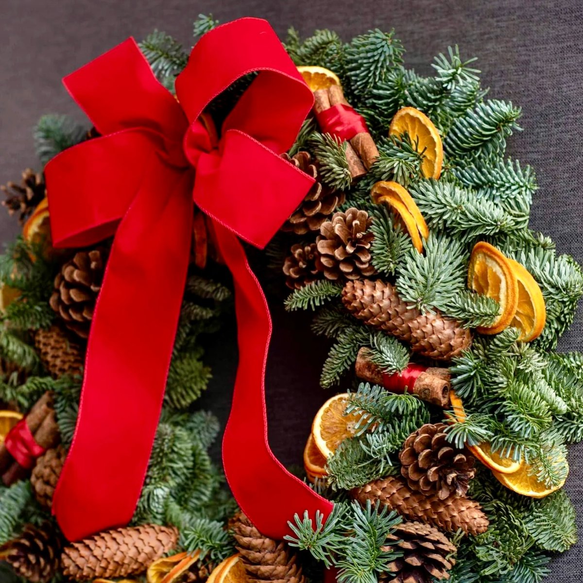 All wrapped up in a red ribbon, the Suffolk wreath is a beautiful creation made from blue spruce pine with natural cones, dried oranges and hand-tied cinnamon clusters. Handmade by our skilled florists in true Pulbrook &amp; Gould tradition.
#PulbrookAndGould #ChristmasWreath