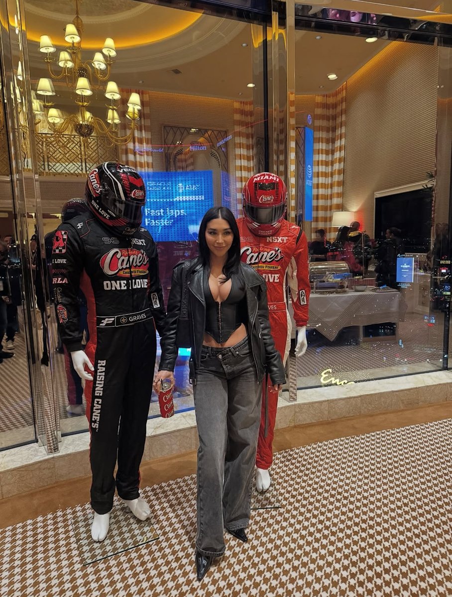 Charlotte brings the edge today as she’s pairing a structured black leather jacket with a sculpted corset top and washed-grey denim for the perfect mix of streetwear and high-fashion. Posed between the race suits, she proves she can outshine any spotlight.