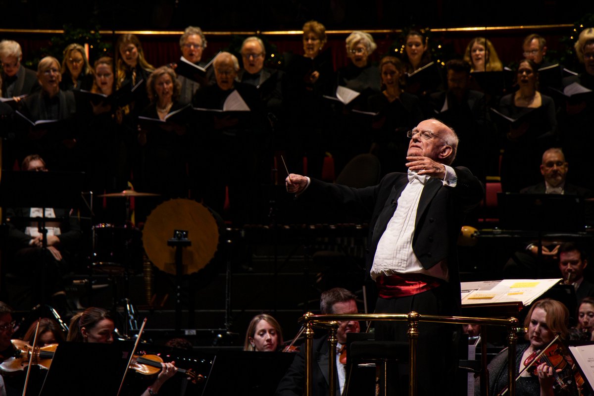John Rutter conducting the audience from the podium with the Orchestra and Bach Choir behind him