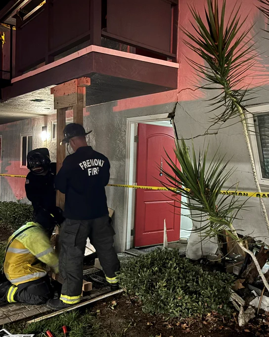 Firefighters in uniform attending to an emergency outside an apartment with caution tape around the entrance.