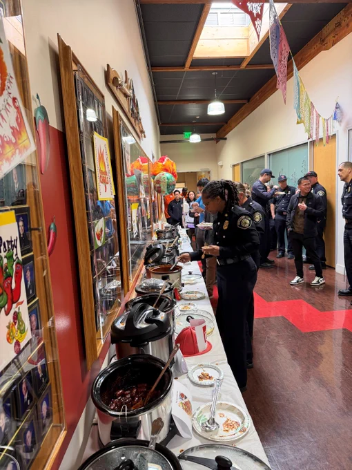 Fire administration serving themselves food from a buffet table in a decorated hallway with colorful banners overhead.