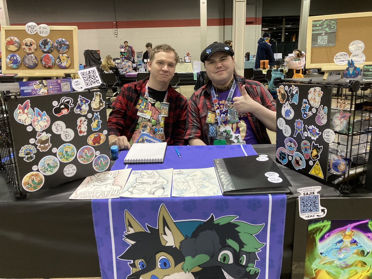 All set up in Artist Alley with <a href="/ArkailArt/">Arkail</a>! 💚💙 We’ve got stickers, buttons, acrylics, and prints, and we’ll be taking sketch commissions later too! Come find us near the front~ (first right when you enter Hall B, halfway down the hall in the central row)