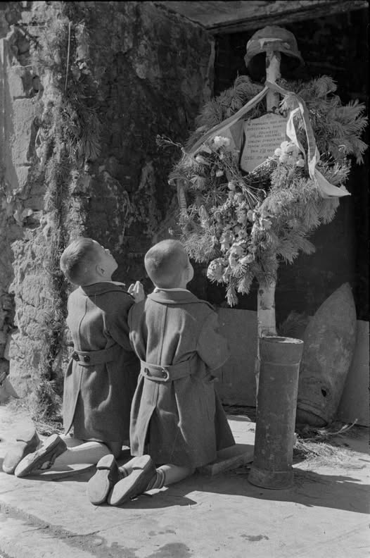 Przejmujące zdjęcie zrobione przez Alfreda Funkiewicza w grudniu 1950 roku.
Na fotografii widzimy dwóch chłopców modlący się pod krzyżem upamiętniającym zamordowanych przez Niemców rannych Powstańców ze szpitala polowego w piwnicy dawnej restauracji „Pod Krzywą Latarnią" przy