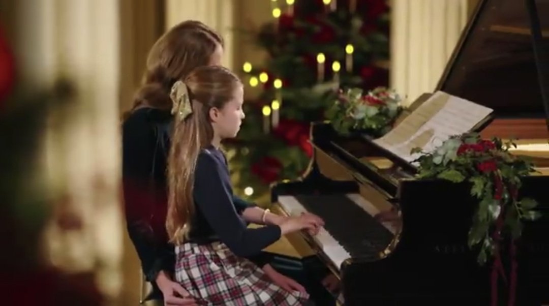 She sits slightly behind and to the side of her daughter, positioned as a supportive mentor ready to assist or comfort her, ensuring Charlotte feels completely supported and at ease while they play together in such a grand, festive event 🫶🏻🤧❤️