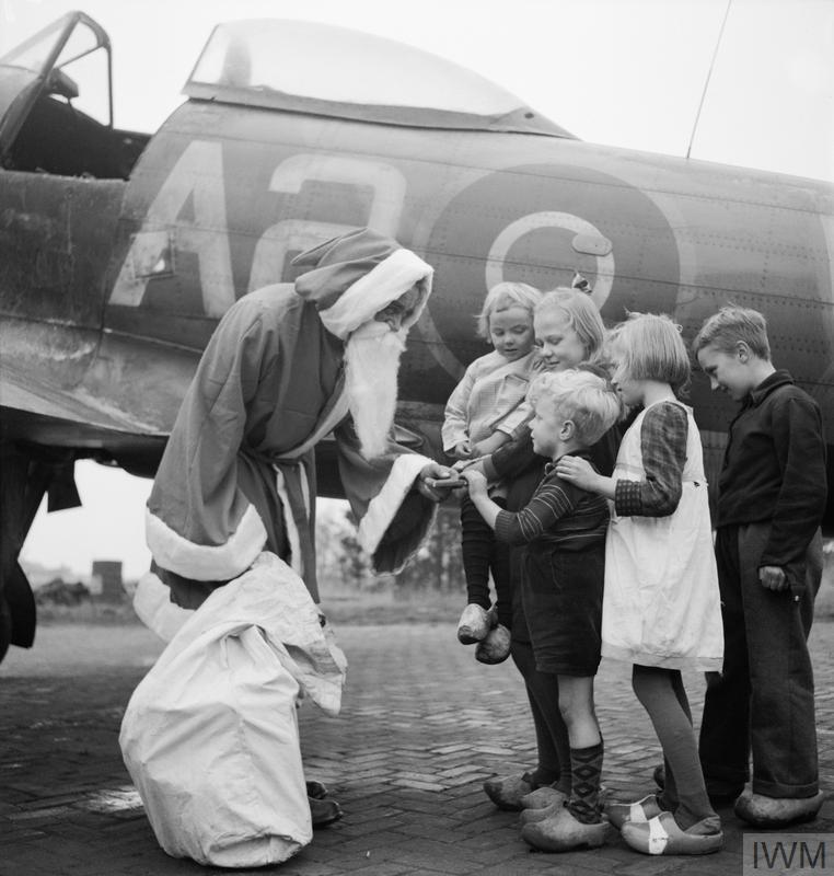 Dressed as Santa Claus, Leading Aircraftman Fred Fazan hands out presents to Dutch children at Volkel, 13 December 1944.

Image: IWM (CL 1729)