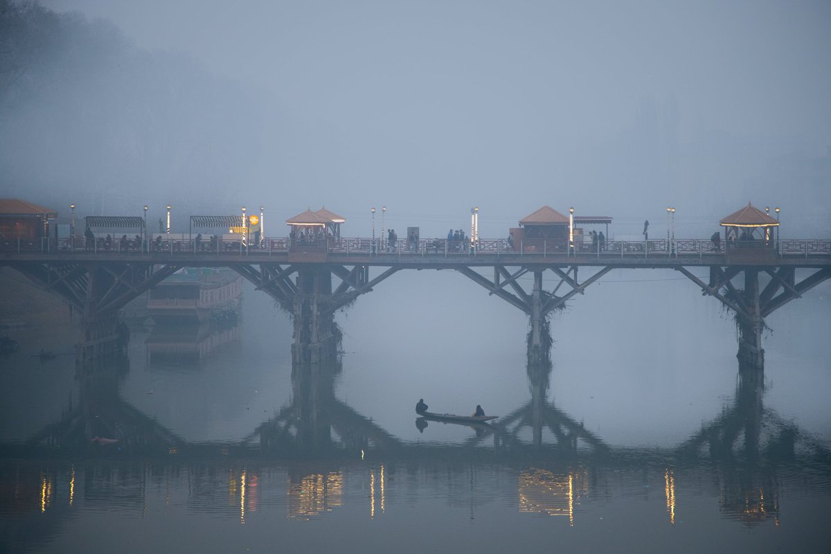 faisalbashirs's tweet image. A #fisherman catches #fish in the #Jhelum #River as #people walk on a #footbridge on a #cold and #foggy #evening in #Srinagar, #Kashmir, #December 13, 2025. Photo by @faisalbashirs