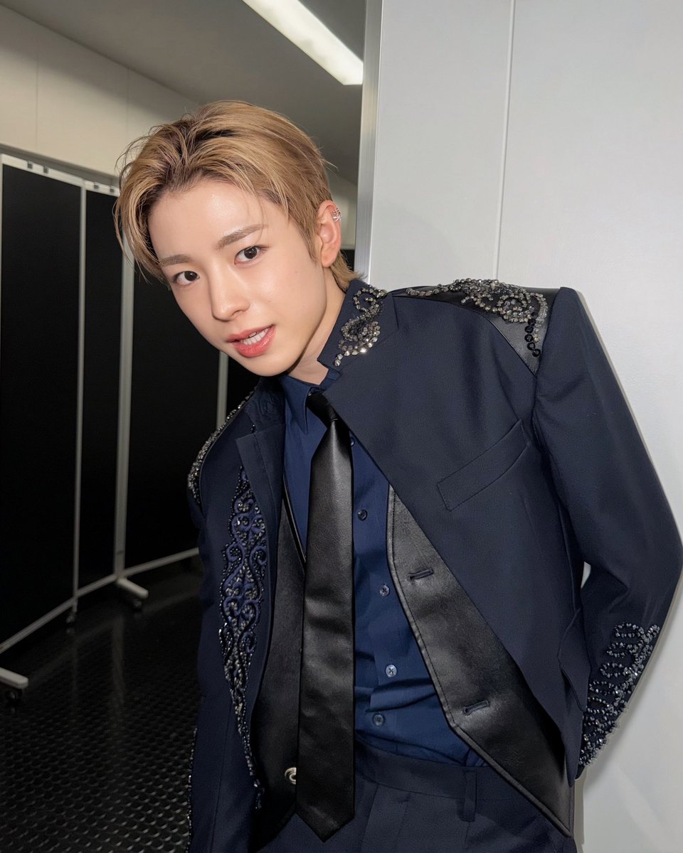 My blonde hair is still perfectly styled from the shoot earlier—side-parted. A little tousled for that effortless vibe, catching the fluorescent light just right. I glance sideways at the mirror, smirking a bit because I know this look is killing it today.