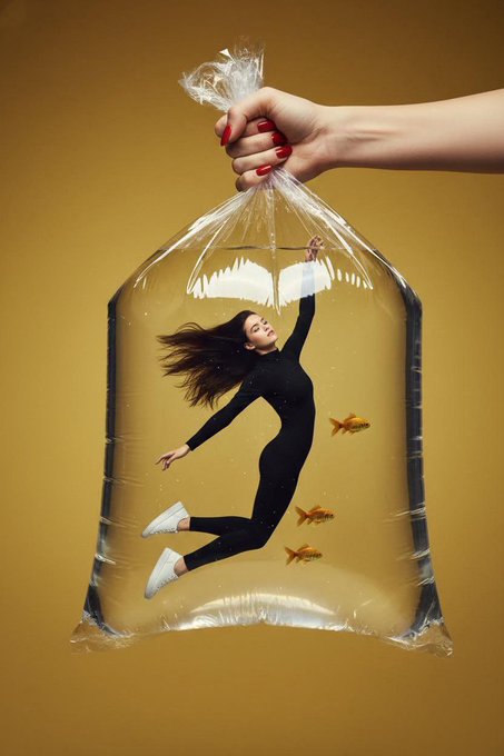 Surreal fashion photograph of a young women floating inside a giant transparent plastic water bag cr