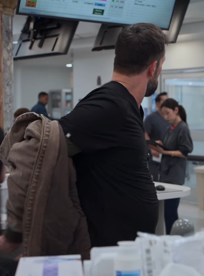 Dennis leaning his elbows on the countertop, slightly bent over as he chats with Dana about something not work related. Robby walks up, and he’s about to tell Dennis to grab another patient, but someone rushes behind and bumps into him. Robby catches himself on whatever is-