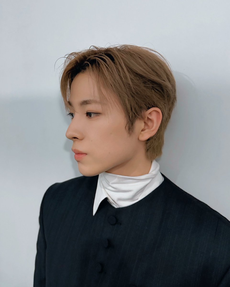 Apollo's chosen son stands where marble gleams like frozen stars, with hair kissed by dawn and eyes bearing the peaceful fire of prophesy. He wears the night itself as armour, with black silk woven from Nyx's own cloak and buttons forged from fallen constellations.