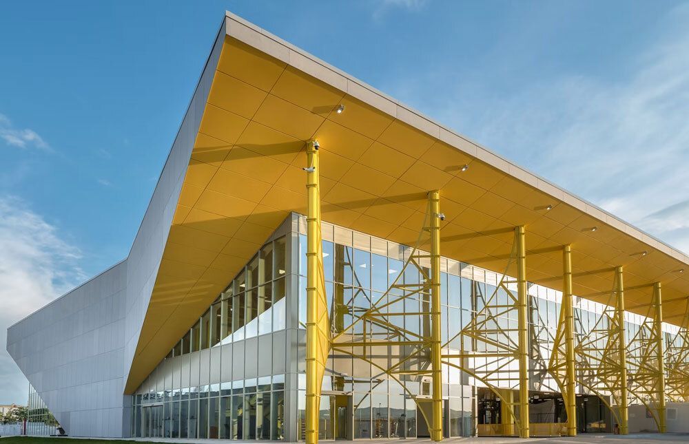 designboom's tweet photo. semi-transparent yellow metal arches frame airport’s terminal extension in romania https://t.co/iohb6PilbS https://t.co/tdpxib8Evl