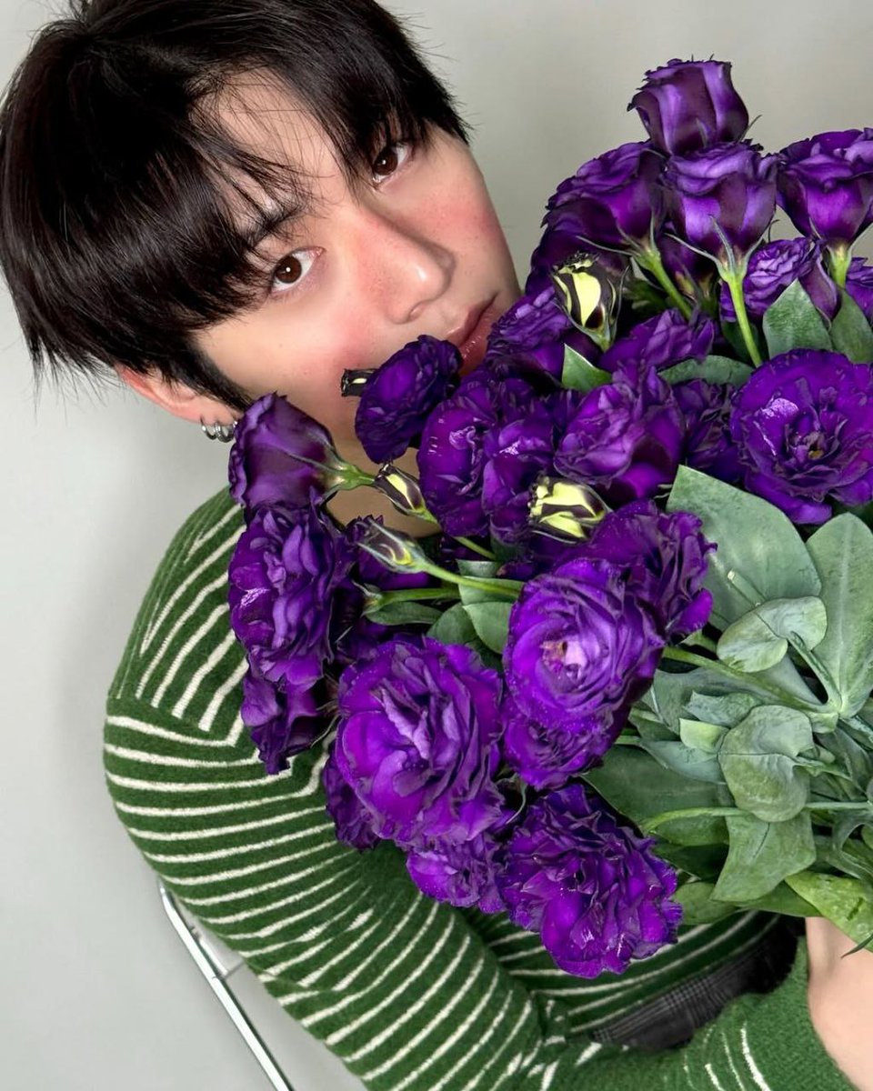 Violet blooms stand as a vow of sincerity, held close against his warm complexion. Their rich tones echo his affectionate appearance, where flowers and essence, offering adoration that feels honest, calm, and deeply genuine.