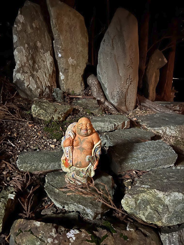 神社の裏山で石碑郡の前に置かれる極彩色の布袋。焚火の明かりで