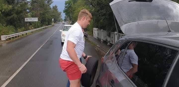 Ndi_Muvenda_'s tweet photo. This young man named Brandon, couldn't let Lerato Thobedi and her 2 friends change a flat tyre by themselves on a busy road. He stopped and got his hands and white Tshirt  dirty in order to change the tyre for them. His white girlfriend did not stop him from helping these ladies either.