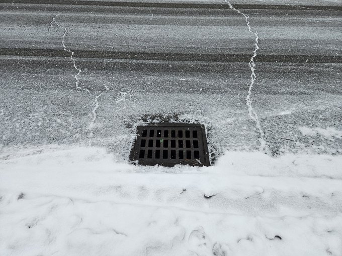 A roadside catch basin with snow around it.