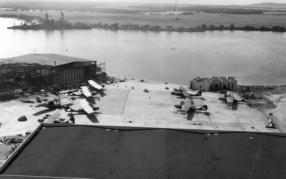 View of Naval Air Station Ford Island on 8 Dec 1941 from the Ford Island water tower. PBY aircraft on the ramp with damaged hangars and the USS Nevada after her move from Hospital Point to the Waipio Peninsula. #PearlHarbor82