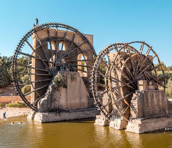 archeohistories's tweet photo. Norias of Hama (Syria); are a collection of historic waterwheels so lovely and elaborate that they make classical Western waterwheels look weak in comparison. Unfortunately, after surviving for hundreds of years, these lovely wooden constructions are in danger of becoming victims of local conflicts.

Evidence of these ornate water wheels dates back as far as the 5th Century CE, although none of the extant examples have been found to be quite so ancient. The norias (“wheels of pots” in Arabic) were originally constructed on the Orontes River to move H2O through a series of aqueducts that fed farms all across the settlement, becoming so iconic that they eventually became the symbol of the city. Even after they fell out of general use with the advent of modern irrigation systems, the norias were left intact, aging into beautiful historic icons of the city’s agrarian past.

By the modern day there were 17 of the historic wheels still standing across the city, some attached to old buildings, others just standing free as city changed around them. The iconic relics were even to be considered protected UNESCO  artifacts, but unfortunately this designation has yet to be approved. Sadly, it may be too late in any event. Recent reports from the war-torn region suggest that some, if not all of the norias may have been burnt down. For history’s sake let’s hope that these reports are greatly exaggerated.

- Subscribe for Weekly Newsletter -
https://t.co/QSjn4yGpeh

#archaeohistories