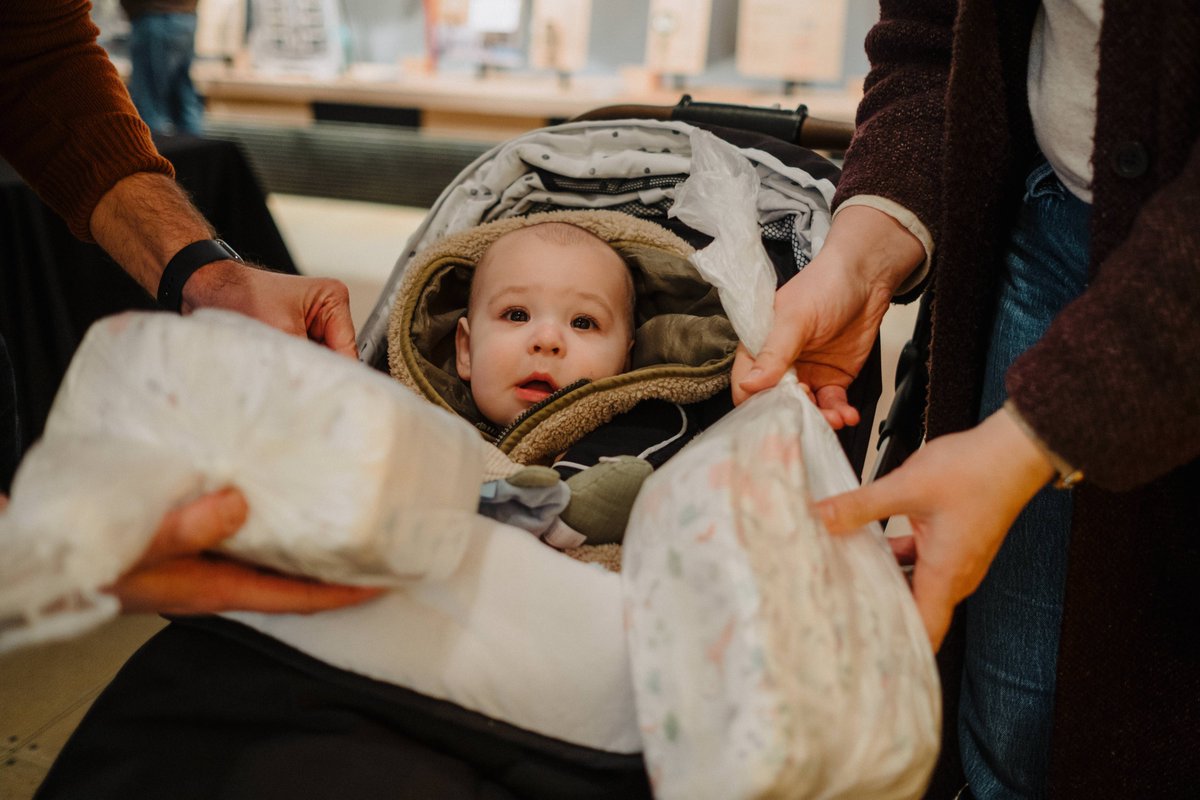 On #GivingTuesday gifts we received ensures all children in our community have access to essential items they need to feel joy this season. Thanks from WestSide Baby 💚 ---- [Image description: A baby with family visiting the WestSide Baby table at an event to donate diapers.]