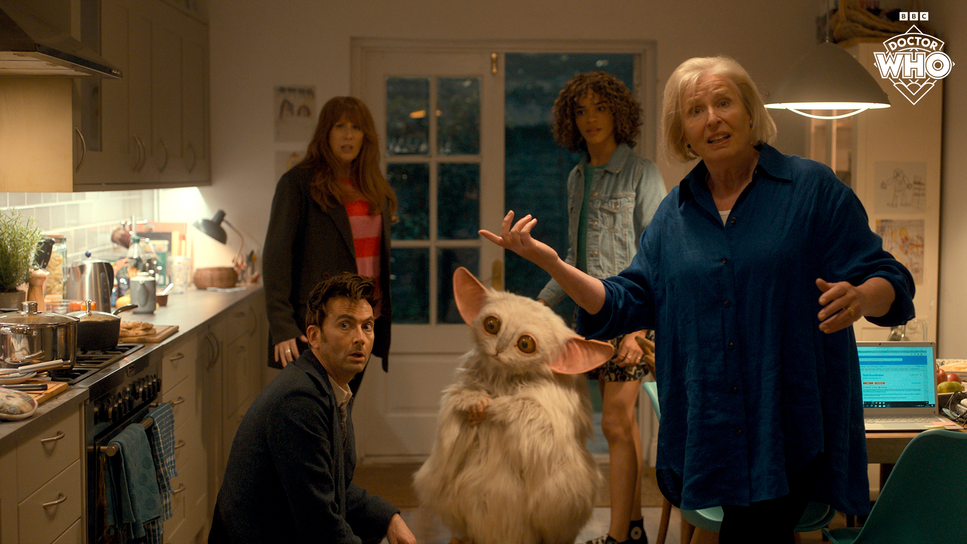 Still from 'The Star Beast' featuring the Doctor, Donna, Rose and Sylvia Noble standing in Donna's kitchen with the Meep.