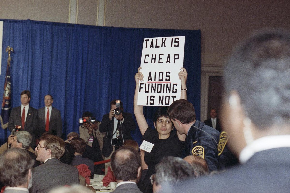 TALK IS CHEAP. AIDS FUNDING IS NOT. #WorldAIDSDay #WorldAIDSDay2023 Urvashi Vaid, then @thetaskforce's executive director, raising a sign over during a speech by President George H. W. Bush to the National Leadership Coalition on AIDS in Virginia, 1990. 📸 @AP / Dennis Cook