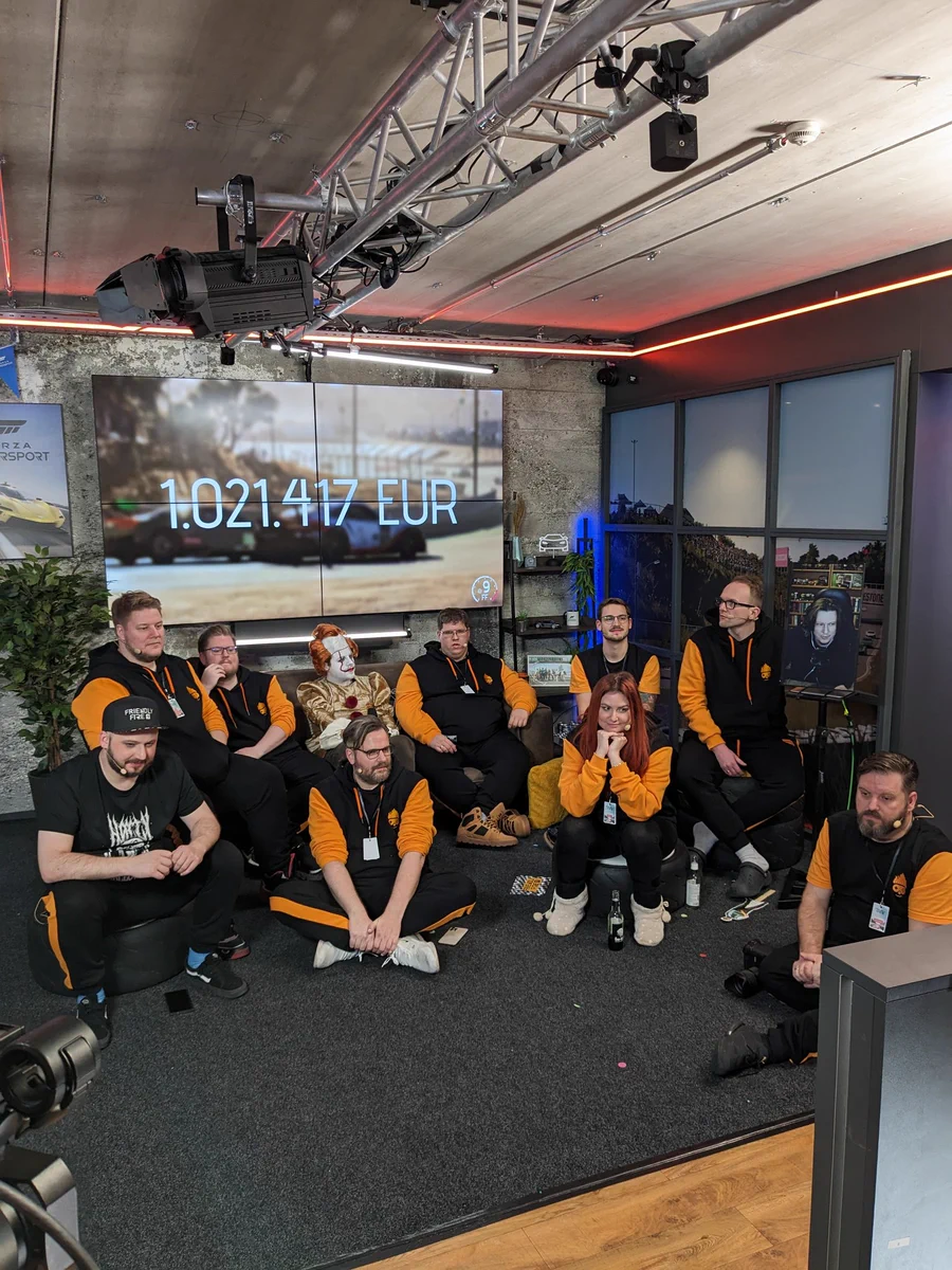 Die Friendly Fire Crew sitzt zur Verabschiedung im Kreis. Im Hintergrund der Spendenstand von 1.021.417 Euro.