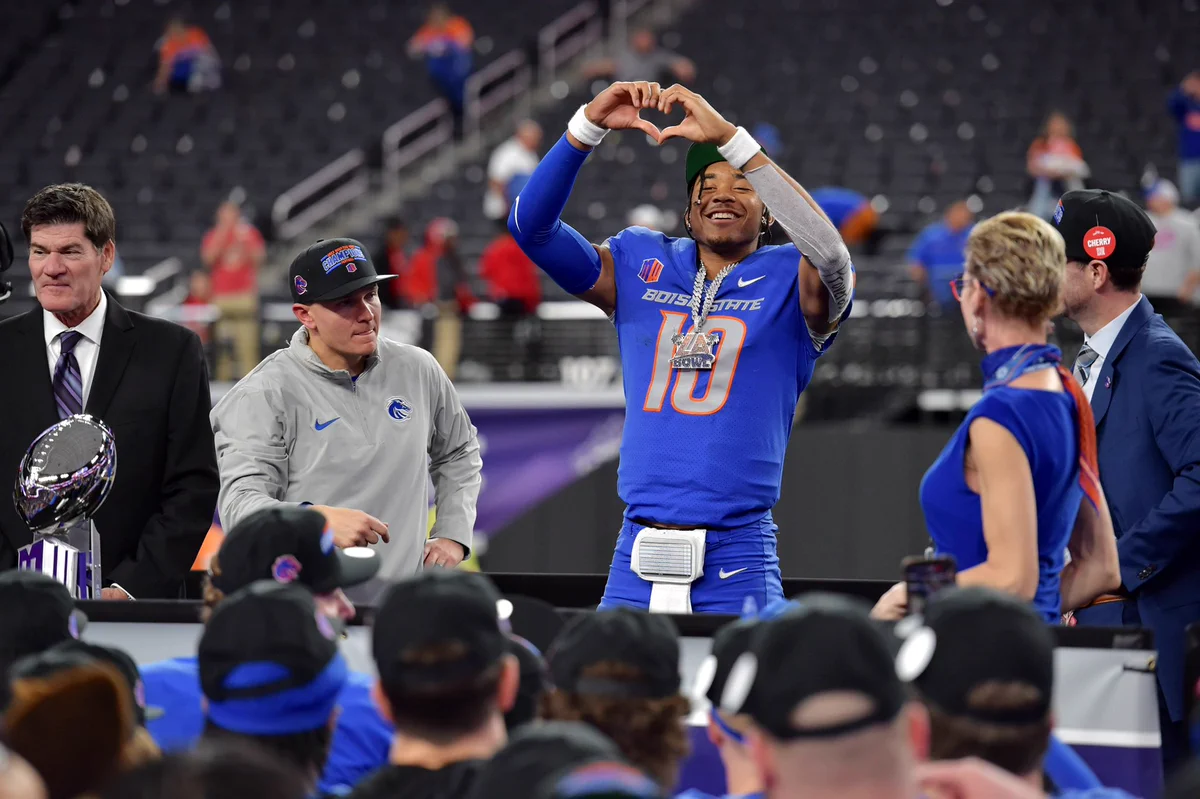 Taylen Green holds hands above head making a heart shape, with Boise State and Mountain West Conference leadership by his side.