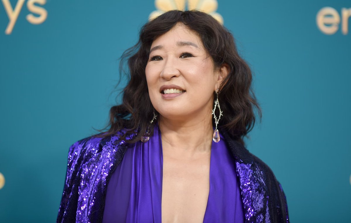 A photo of Sandra Oh wearing a purple jacket and blouse walking a red carpet.