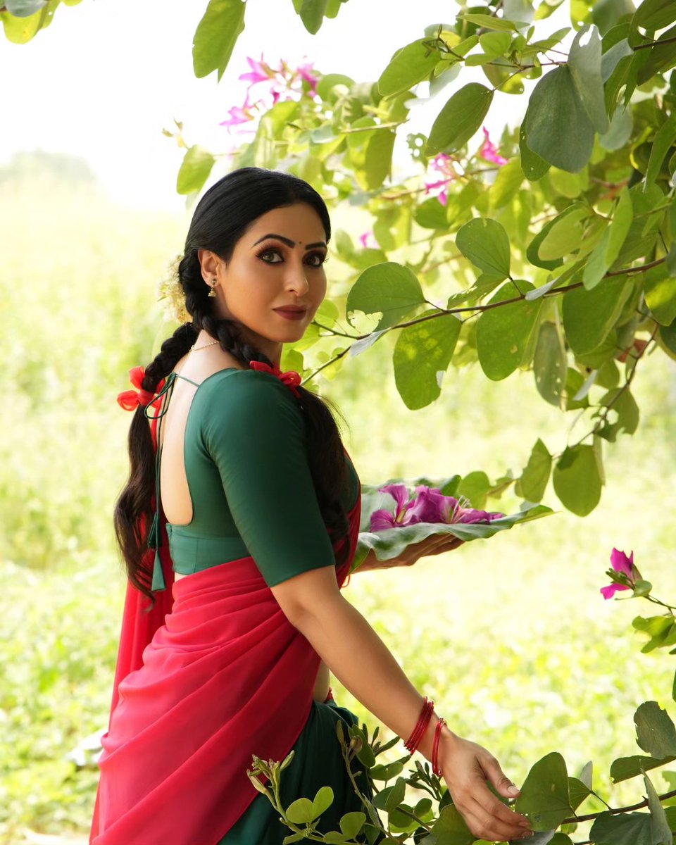 Captivating colors and timeless elegance come together in this stunning image of a woman in a vibrant green and red sari, gracefully holding a delicate flower. The rich cultural heritage and natural beauty are beautifully captured in this moment of serene and captivating harmony