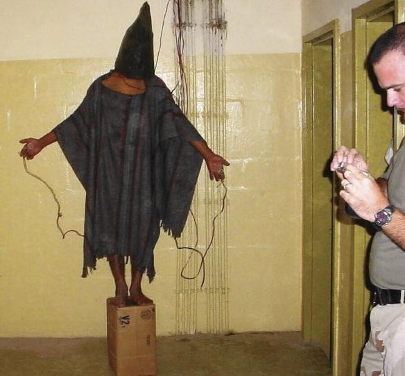 creepydotorg's tweet photo. An inmate being tortured at Abu Ghraib Prison by US forces. He had electric wires attached to him and was told that if he fell off the box, he would be electrocuted. November, 2003. https://t.co/mIxMj76ePP