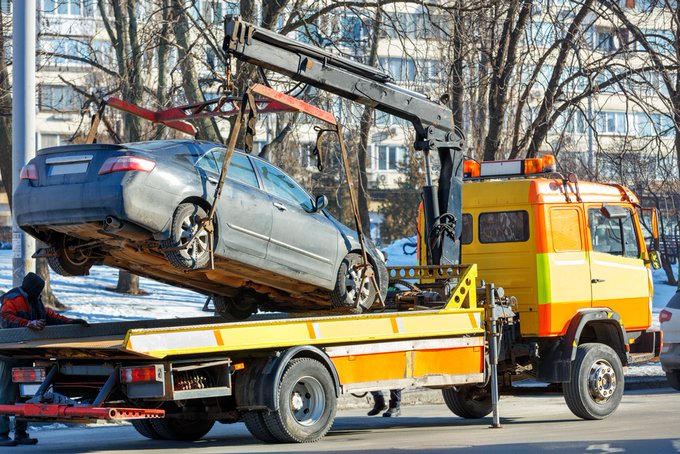 A broken-down car being hoisted onto the bed of a tow truck on a city street.