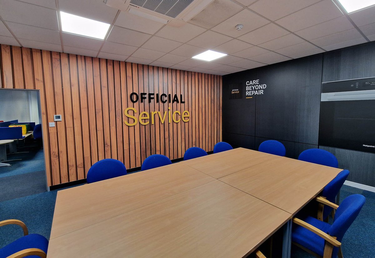 Wood effect printed wallpaper with OFFICIAL SERVICE added in acrylic lettering raised from the wall, alongside a second printed wallpaper complementing each other with striking effect for this boardroom at the Whirlpool offices in Peterborough. #officespaces #wallpaperdesigns