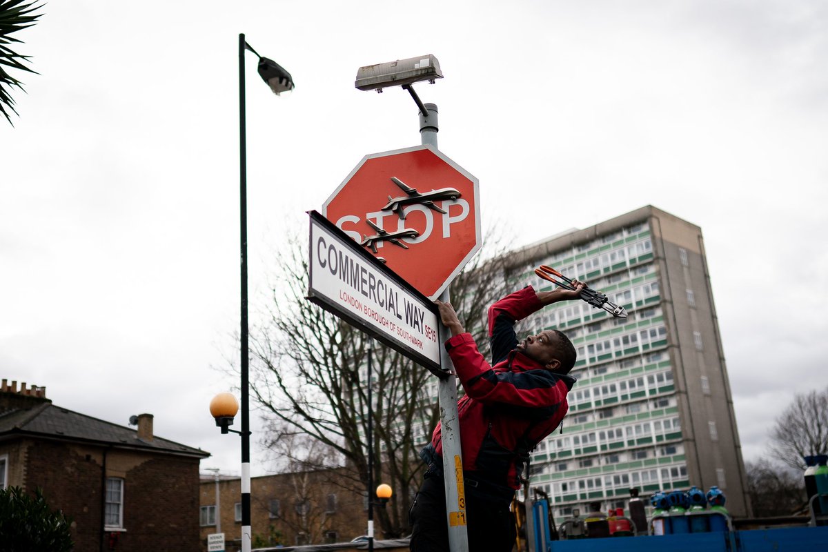 People remove a piece of art work by Banksy, which shows what looks like three drones on a traffic stop sign, which was unveiled at the intersection of Southampton Way and Commercial Way in Peckham, south east London.