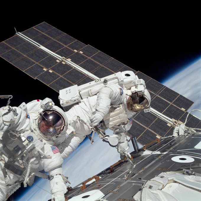 Astronauts Jerry L. Ross (left) and James H. Newman, both mission specialists, work together on the final of three space walks of the STS-88 mission. One of the solar panels of the Russian-built Zarya module runs through the frame and the Earth and the blackness of space can be seen in the background.