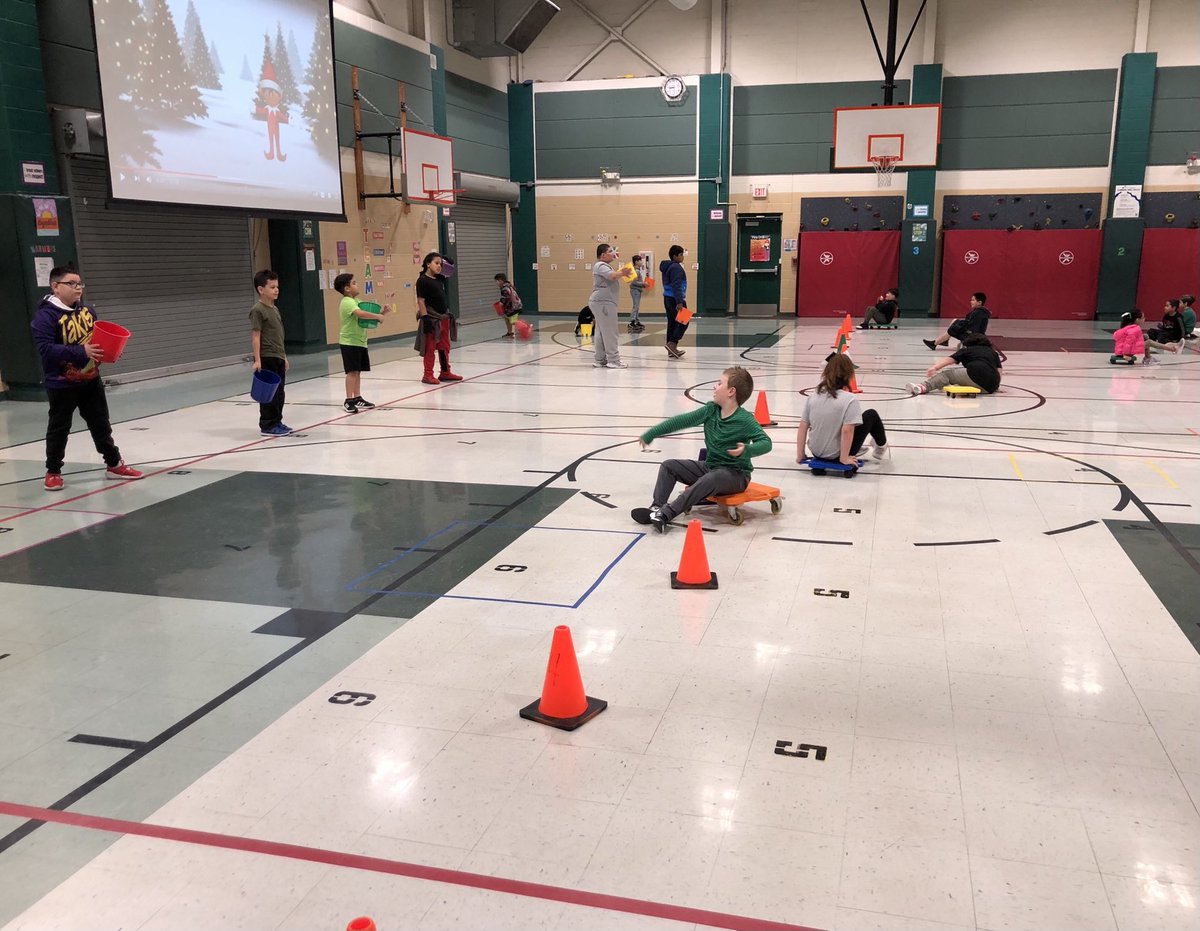 ⁦<a href="/NISDRhodes/">Rhodes Elementary</a>⁩ Raptor 3rd graders were helpful elves by working their throwing/catching skills with scooters. Ss ride scooters down to cone then throw beanbag/present into bucket. ⁦<a href="/NISD_PE/">NISD PE</a>⁩ #teamwork
