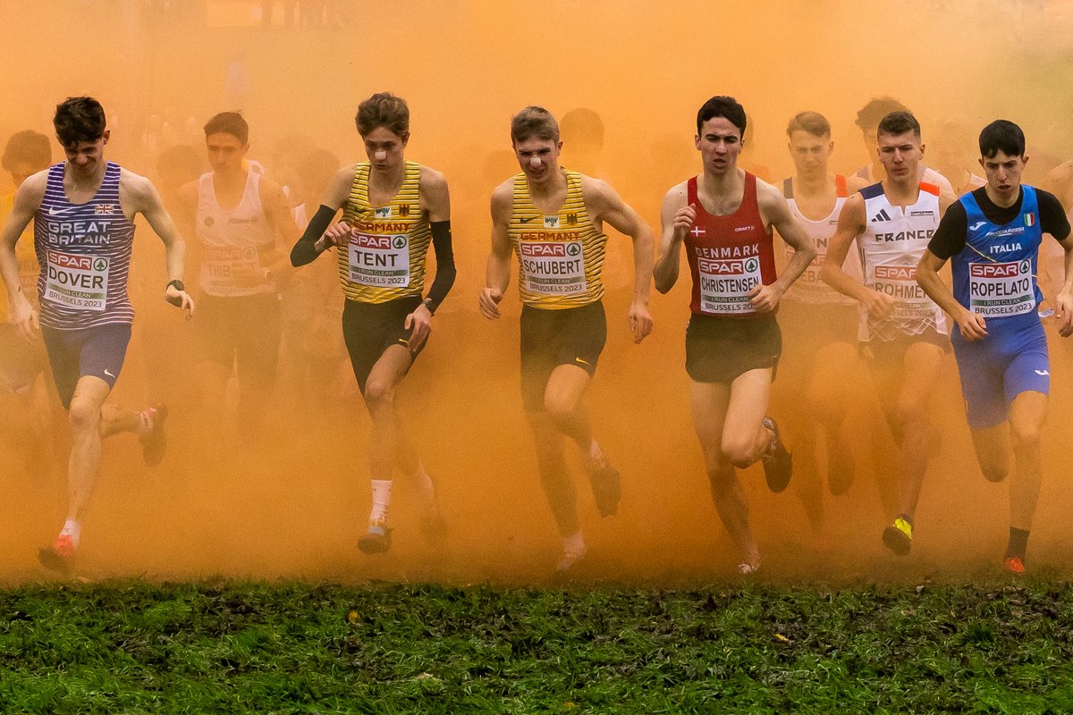 Competitors in the @europeanathletics Cross Country Champions run through coloured smoke at the start of the Men's U20 race at Laeken Park Brussells