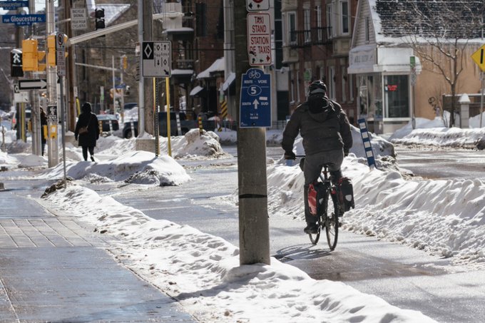 Un cycliste circule sur une piste cyclable près d’une rue urbaine en hiver. 