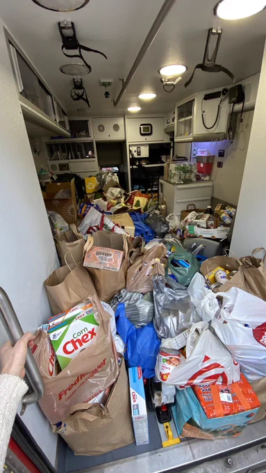 Bags and boxes of donated nonperishable foods completely fill the inside of an ambulance. The floor and seats are not visible.
