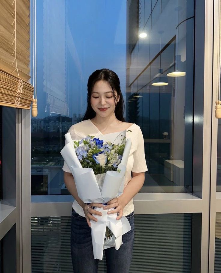 A beautiful woman with a sweet smile adorned in a plain white dress holding beautiful flowers in her hands.