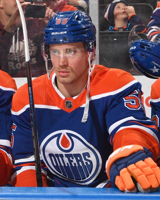 Dylan Holloway is pictured sitting on the bench at Rogers Place in a royal blue home jersey.
