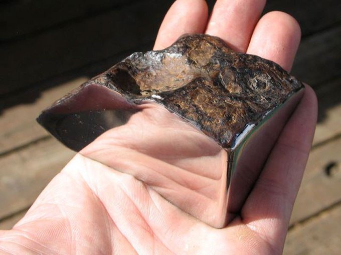 This is a 773 gram polished Chinga meteorite. 

The quarter-cut specimen was found in Turvinskaya, Russia and has been cut and polished on two sides. The rest of the meteorite retains its natural light brown crust, creating a dramatic contrast.