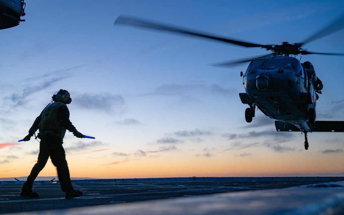 Chasing the sunset on this #SunsetSunday 🚁 ☀️ Aviation Boatswain’s Mate 1st Class Reyvin Olaes, signals to Sailors assigned to the San Antonio-class amphibious transport dock ship USS Somerset as they remove chocks and chains from an MH-60S Sea Hawk. 📸: MC2 Evan Diaz