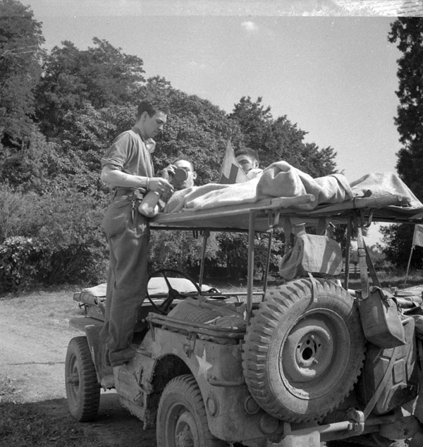 Private H. Hackett of the 18th Field Ambulance, Royal Canadian Army Medical Corps (R.C.A.M.C.), offers a drink to Sapper K.J. Pratt, Bourgtheroulde, France, 26 August 1944.