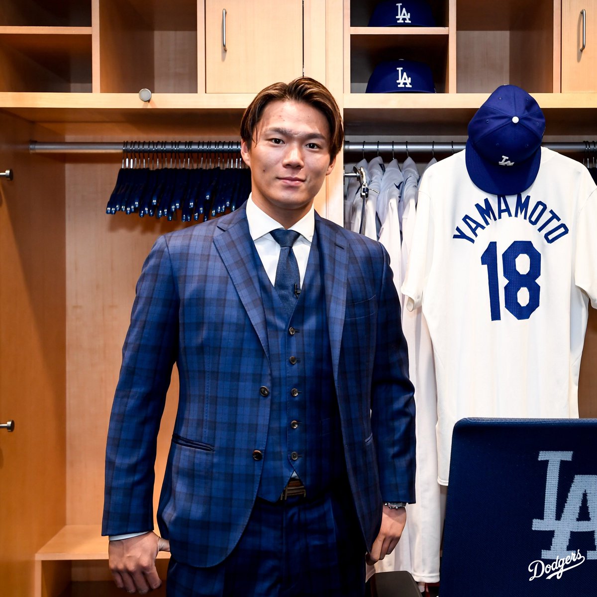 Yoshinobu Yamamoto poses in front of his locker with his new 18 jersey hanging up to the right.
