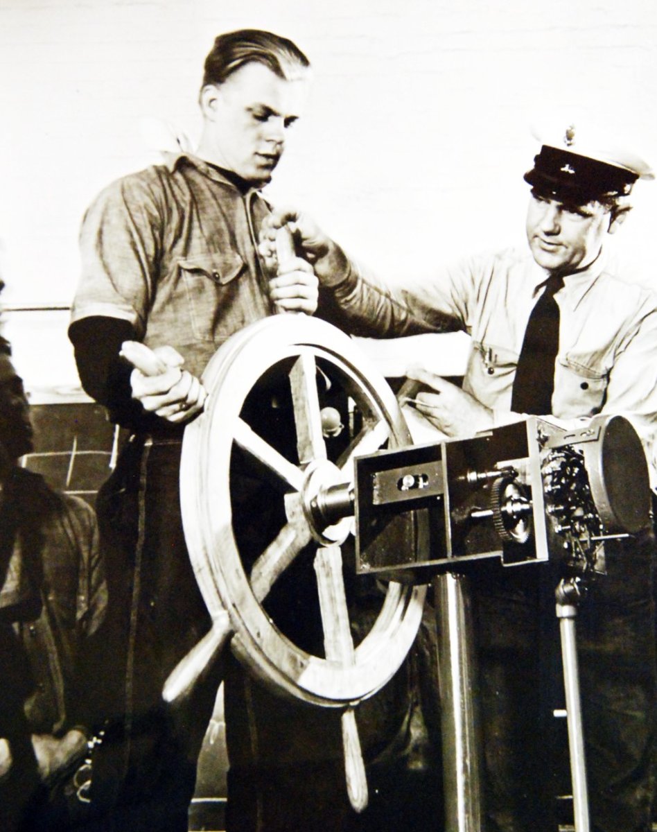 Correct methods of steering the ship and handling the wheel are explained to an apprentice seaman by a petty officer at a training center established by the U.S. Maritime Service on the Pacific Coast.  history.navy.mil/content/histor…
