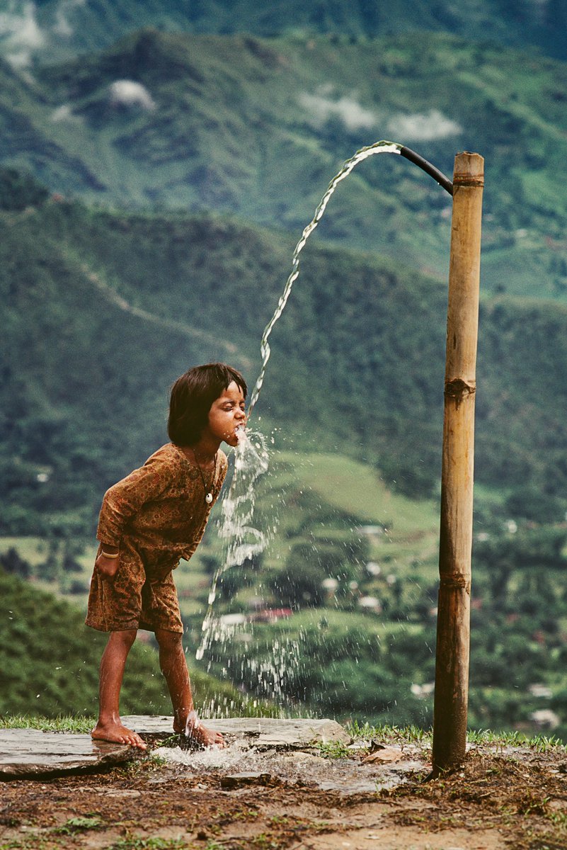 Child drinks water from well, Nepal, 1983 - by Steve McCurry (1950), American